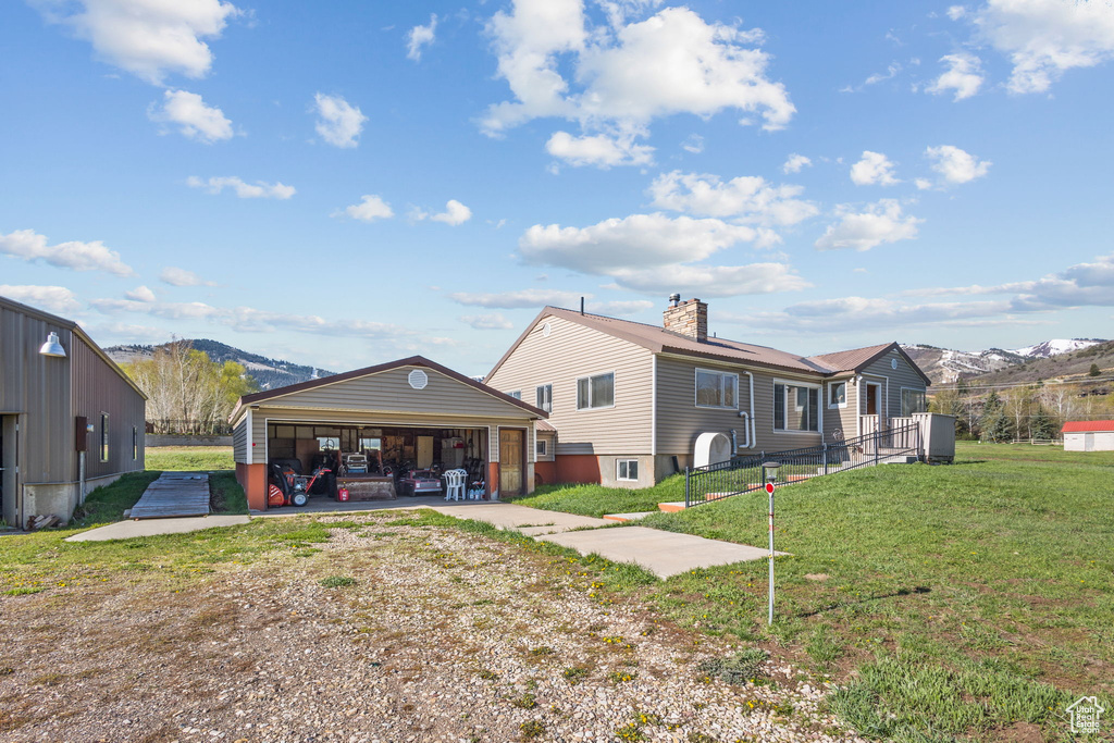 Back of house with a garage, a chimney, a lawn, a mountain view, and an outbuilding