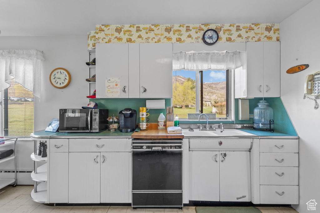 Kitchen with a sink, light countertops, black appliances, and white cabinetry