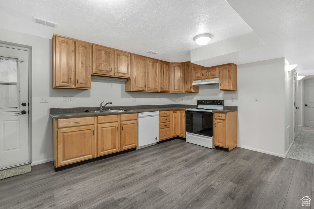 Kitchen with range with electric cooktop, dark countertops, dishwasher, a sink, and under cabinet range hood