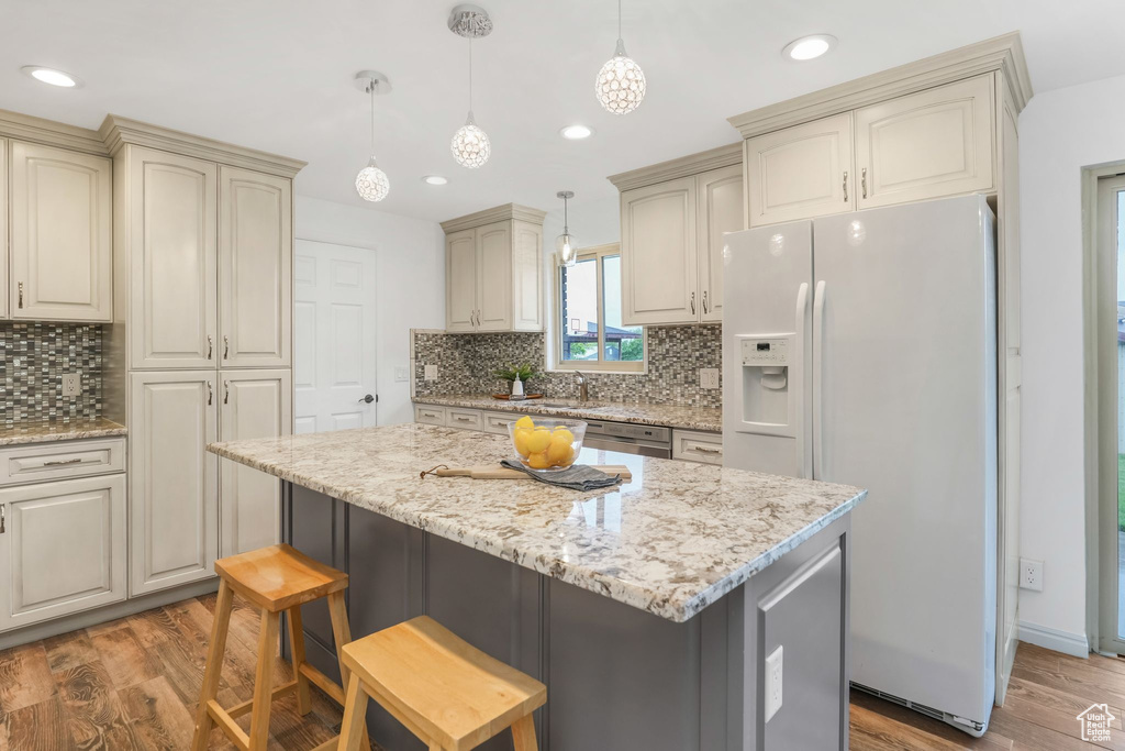 Kitchen featuring cream cabinetry, light wood finished floors, backsplash, and white refrigerator with ice dispenser