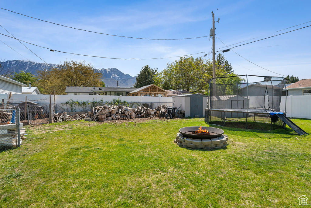 View of yard featuring an outdoor structure, a fenced backyard, a storage unit, a trampoline, and an outdoor fire pit