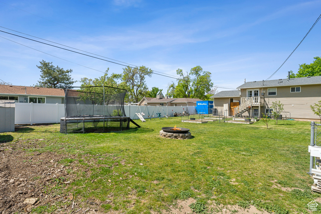 View of yard featuring a fenced backyard, a trampoline, stairs, and a fire pit