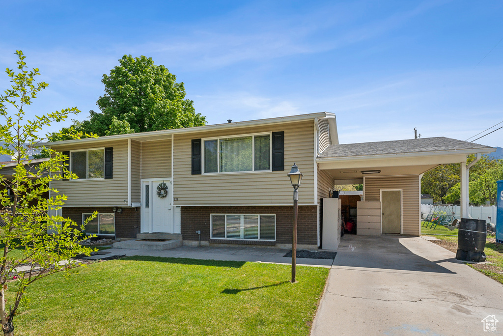 Raised ranch with fence, brick siding, an attached carport, a front yard, and concrete driveway