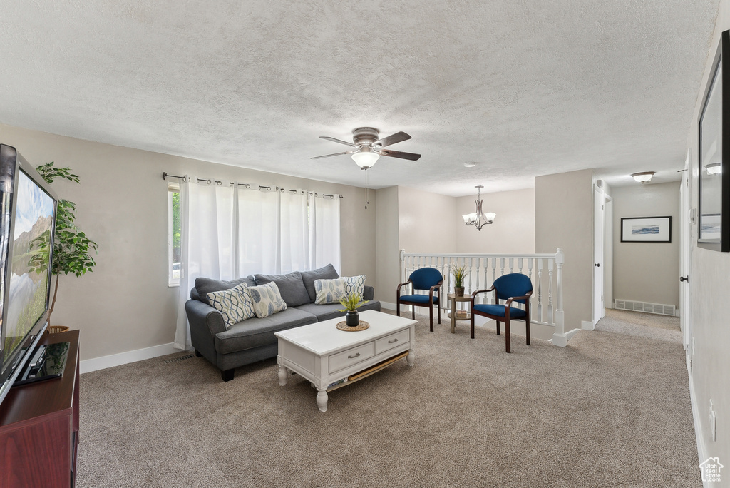 Living area featuring visible vents, a textured ceiling, ceiling fan with notable chandelier, and light carpet