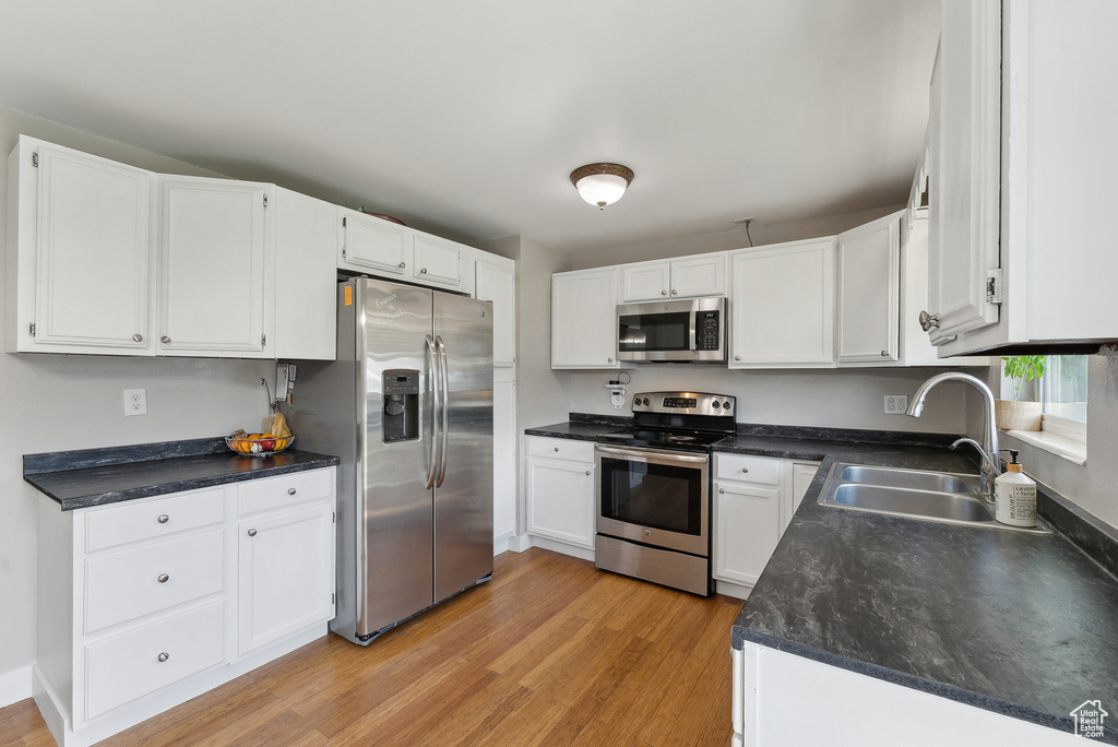 Kitchen featuring a sink, stainless steel appliances, light wood finished floors, and white cabinetry
