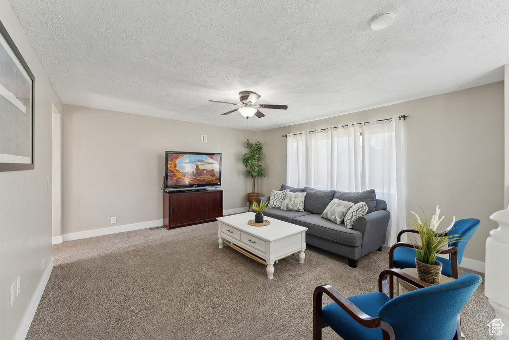 Living area featuring baseboards, ceiling fan, a textured ceiling, and light colored carpet