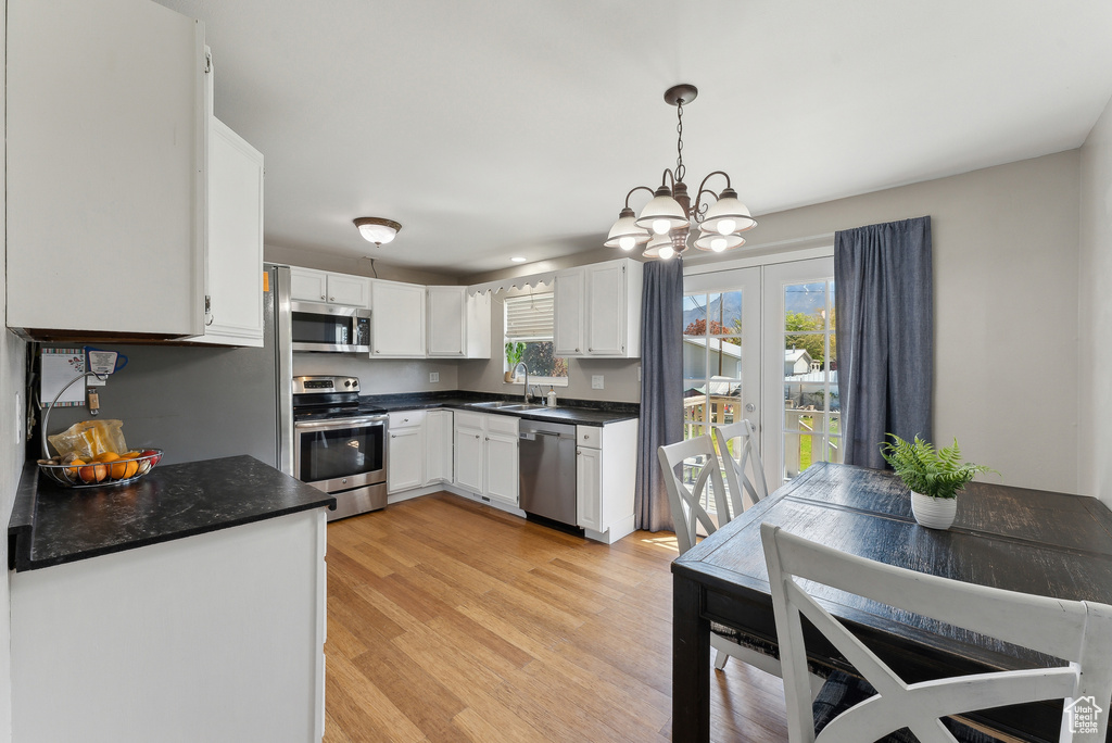 Kitchen with dark countertops, a sink, light wood finished floors, stainless steel appliances, and white cabinetry