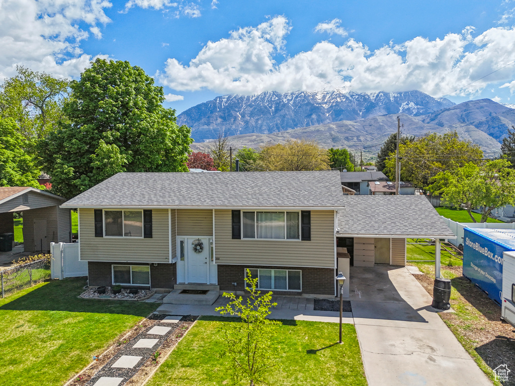 Raised ranch with fence, brick siding, an attached carport, a front yard, and driveway