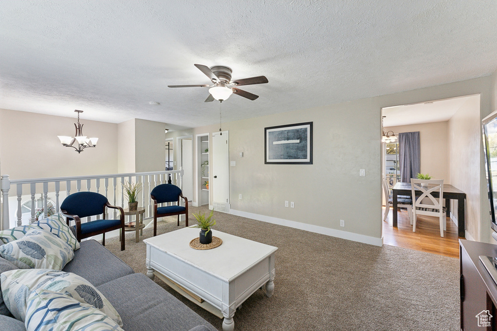 Living room featuring baseboards, light carpet, ceiling fan with notable chandelier, and a textured ceiling
