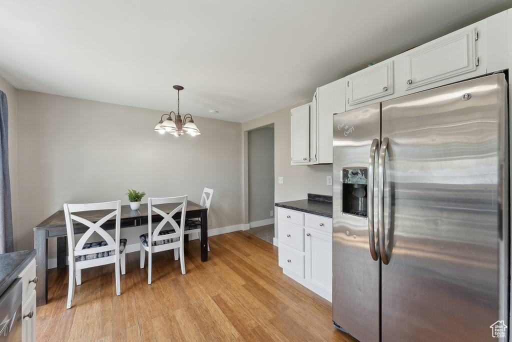 Kitchen with white cabinets, dark countertops, an inviting chandelier, stainless steel fridge with ice dispenser, and light wood-style flooring