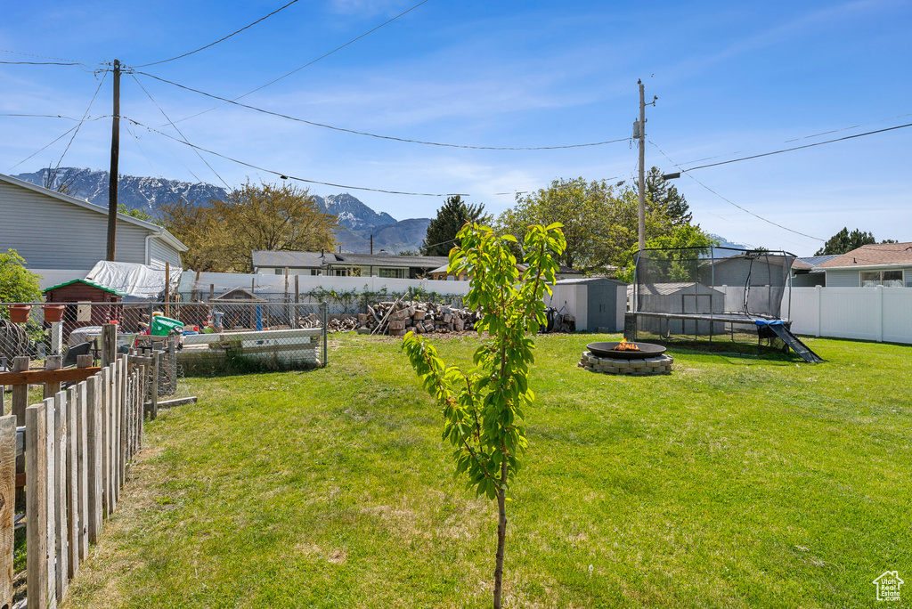 View of yard with a trampoline, a storage shed, a fenced backyard, a mountain view, and an outdoor structure
