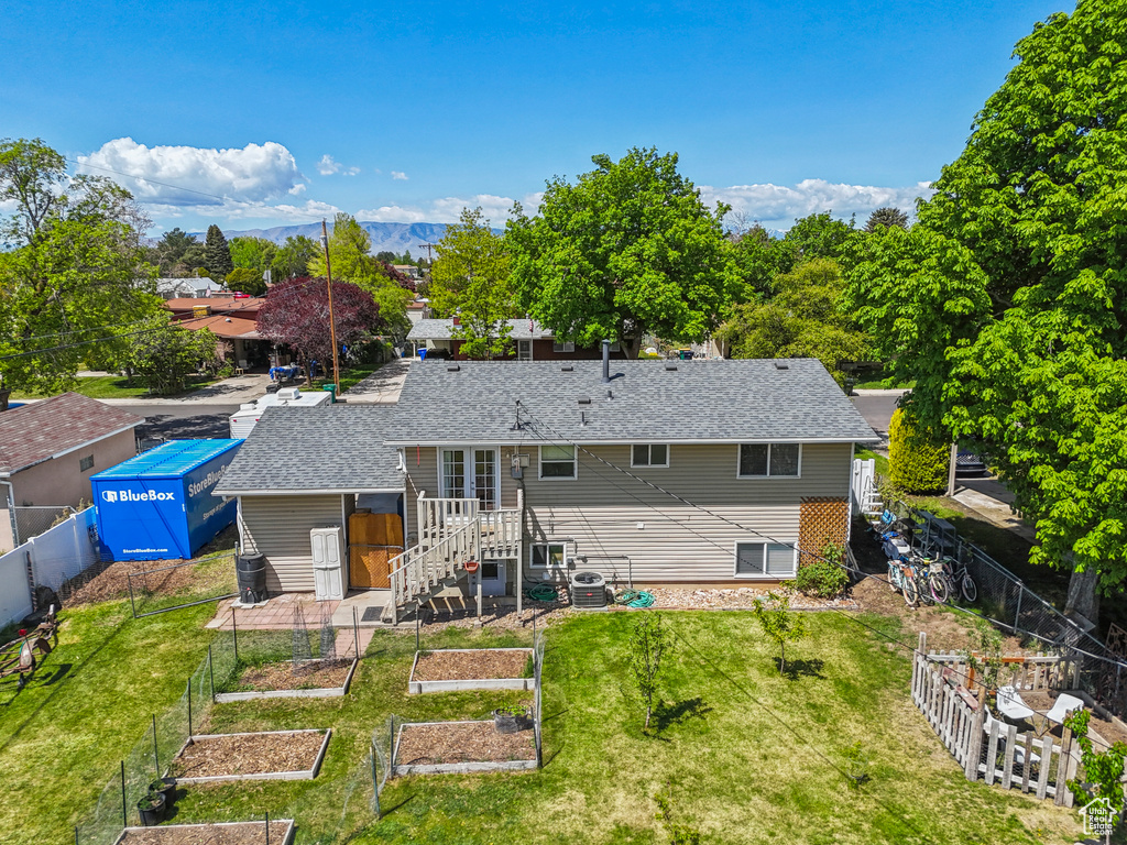 Back of house with a fenced backyard, roof with shingles, a yard, and a vegetable garden