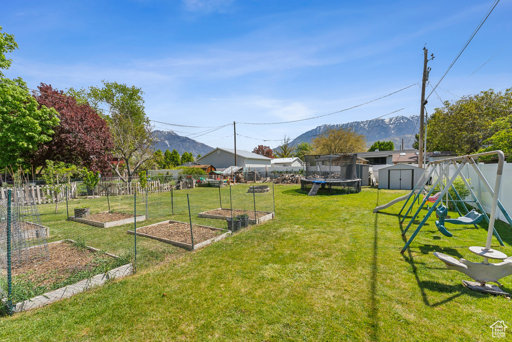 View of yard with a trampoline, a shed, a mountain view, an outbuilding, and a garden