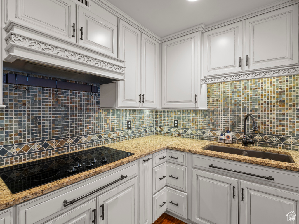 Kitchen with a sink, custom exhaust hood, white cabinetry, and black electric cooktop