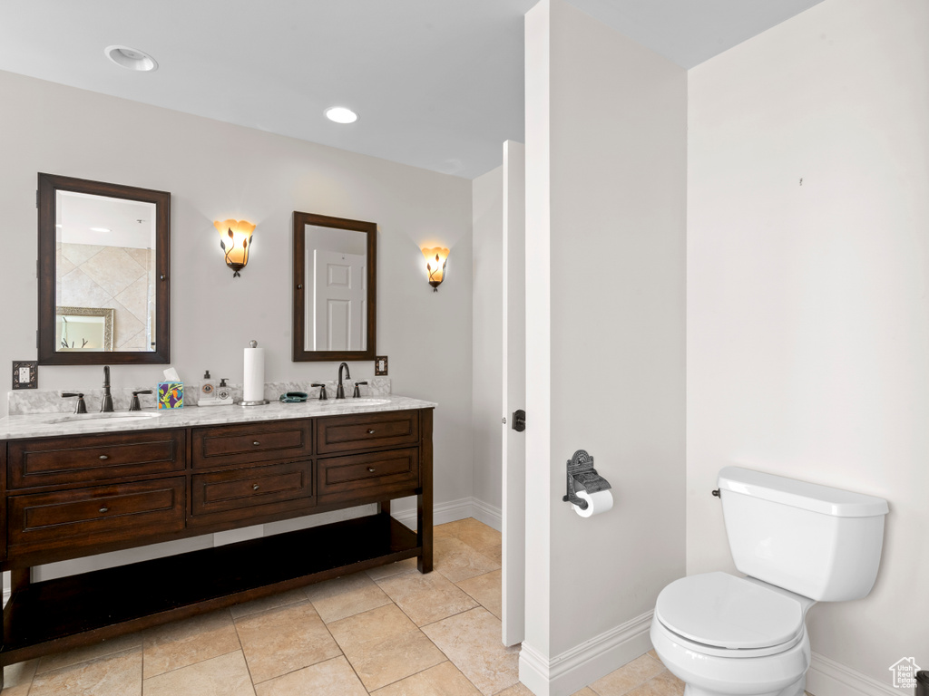 Bathroom with double vanity, toilet, baseboards, and a sink