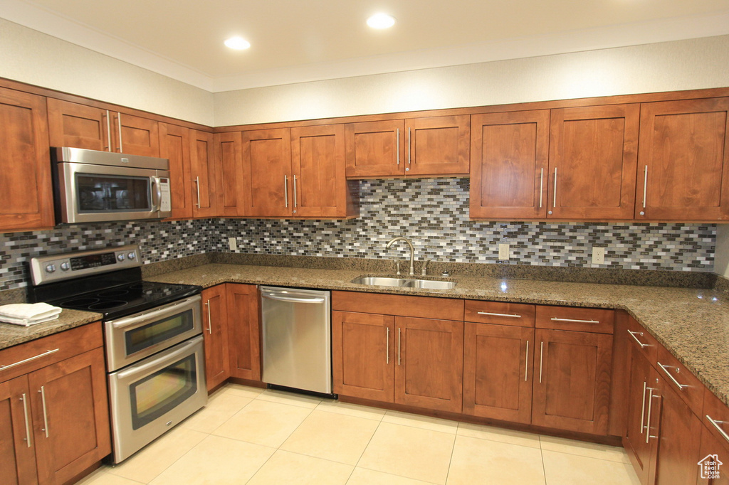Kitchen with a sink, dark stone countertops, backsplash, light tile patterned floors, and stainless steel appliances