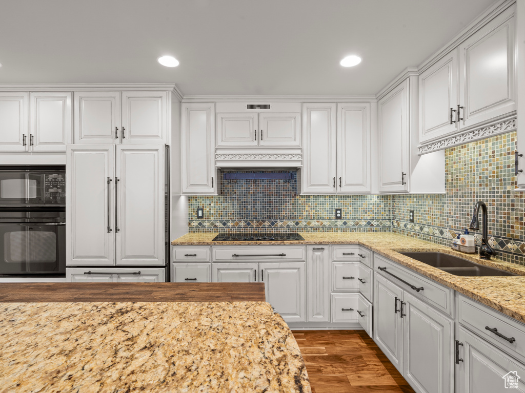 Kitchen featuring white cabinetry, a sink, black appliances, and tasteful backsplash