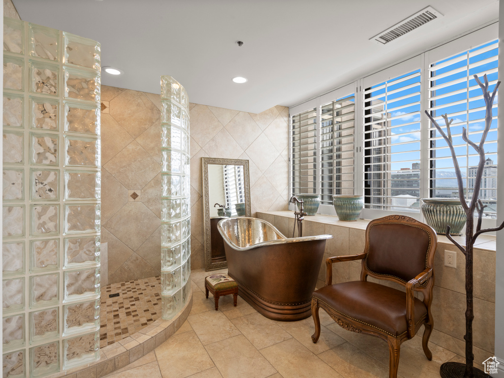 Bathroom with plenty of natural light, visible vents, tile walls, a walk in shower, and a soaking tub