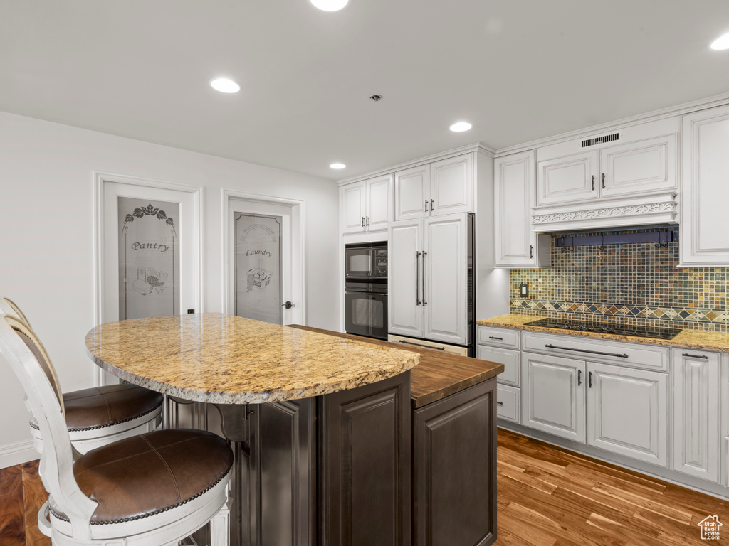 Kitchen with visible vents, a center island, white cabinets, black appliances, and light wood-style floors
