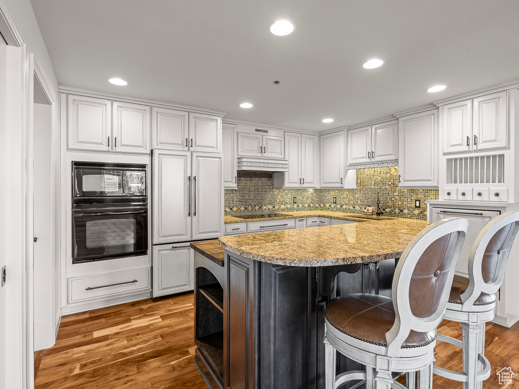 Kitchen with white cabinets, a kitchen island, black appliances, and light wood-type flooring