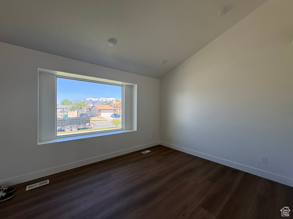 Unfurnished room with baseboards, dark wood-style flooring, vaulted ceiling, and visible vents
