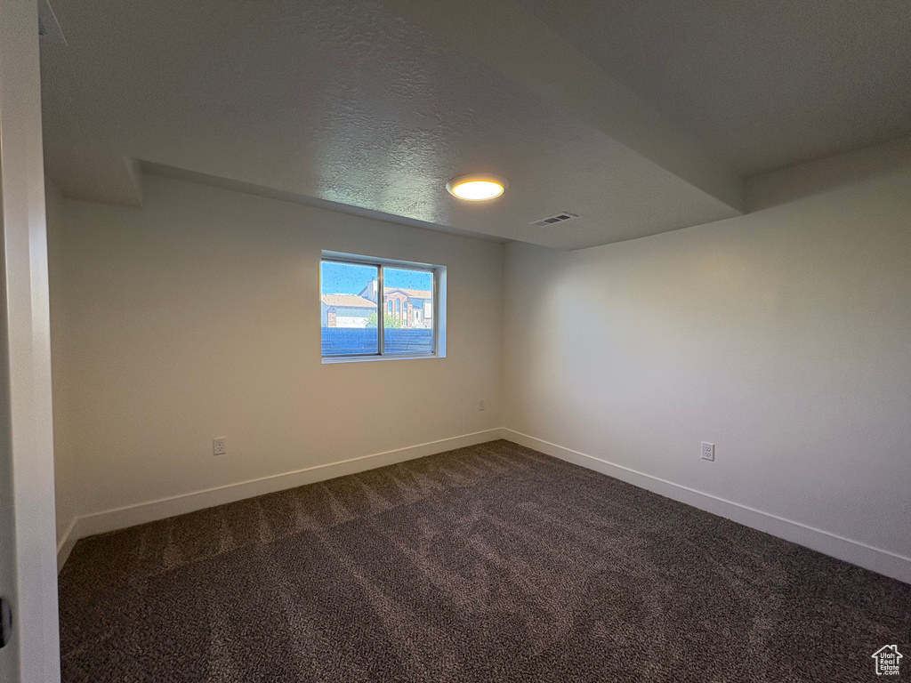 Unfurnished room with baseboards, visible vents, and dark carpet