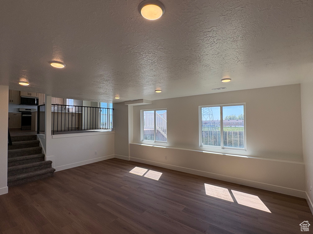 Unfurnished living room featuring dark wood-style flooring, baseboards, and visible vents