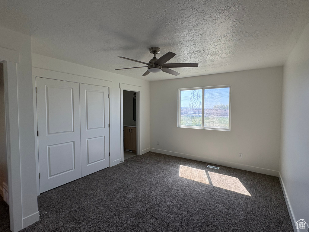 Unfurnished bedroom with a textured ceiling, baseboards, visible vents, and dark colored carpet