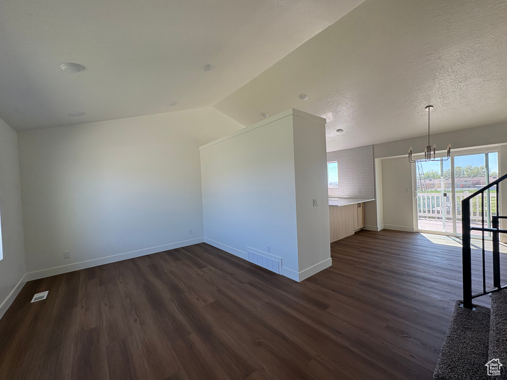 Additional living space featuring visible vents, dark wood finished floors, baseboards, lofted ceiling, and an inviting chandelier