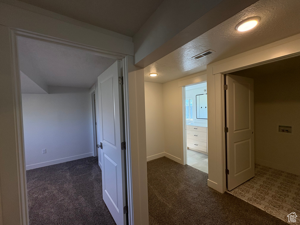 Corridor with carpet floors, a textured ceiling, baseboards, and visible vents