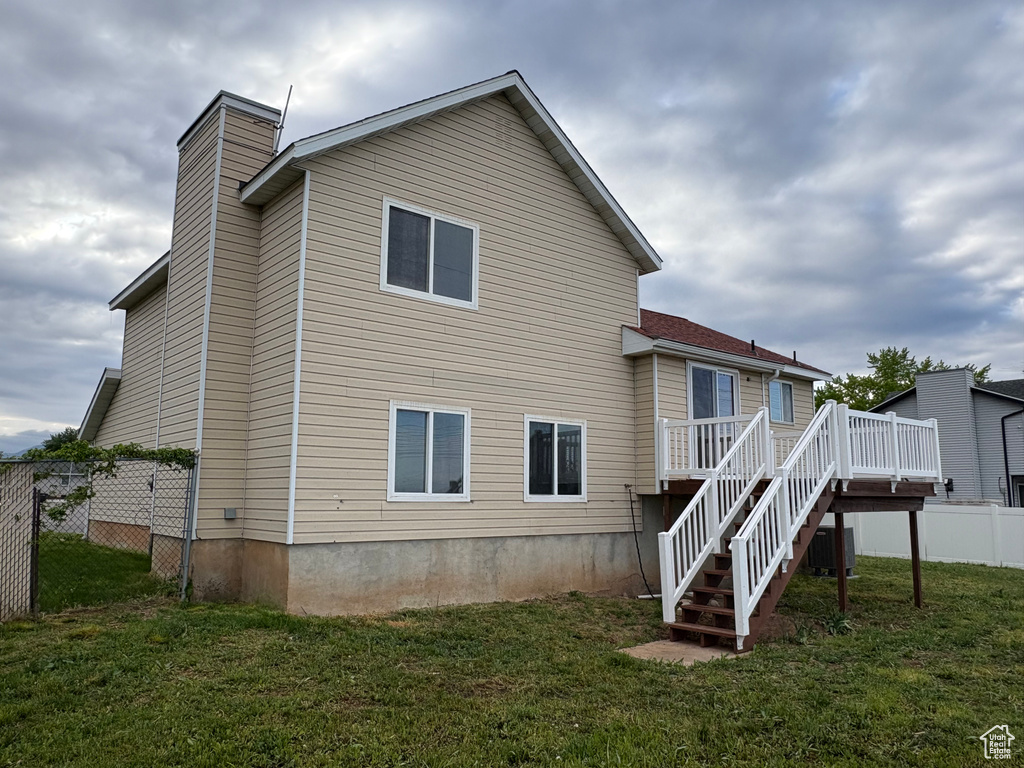 Back of property featuring a chimney, a lawn, fence, a wooden deck, and stairs