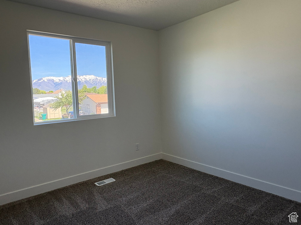 Spare room with baseboards, a mountain view, dark colored carpet, and visible vents