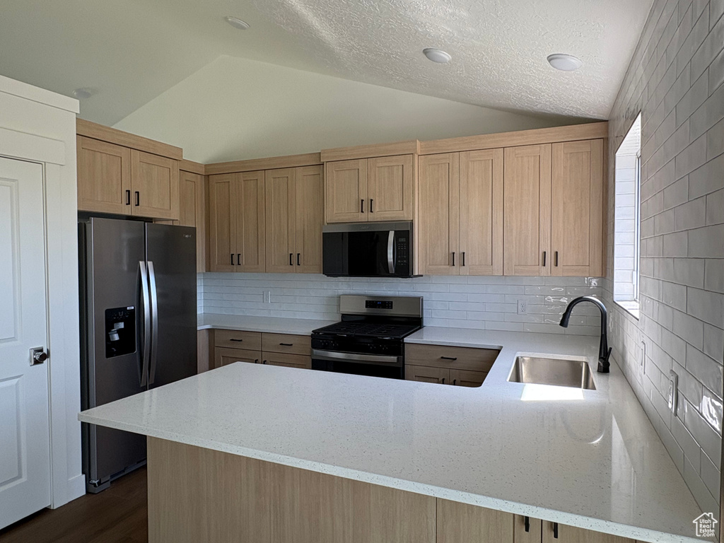 Kitchen featuring a peninsula, light brown cabinets, a sink, appliances with stainless steel finishes, and vaulted ceiling