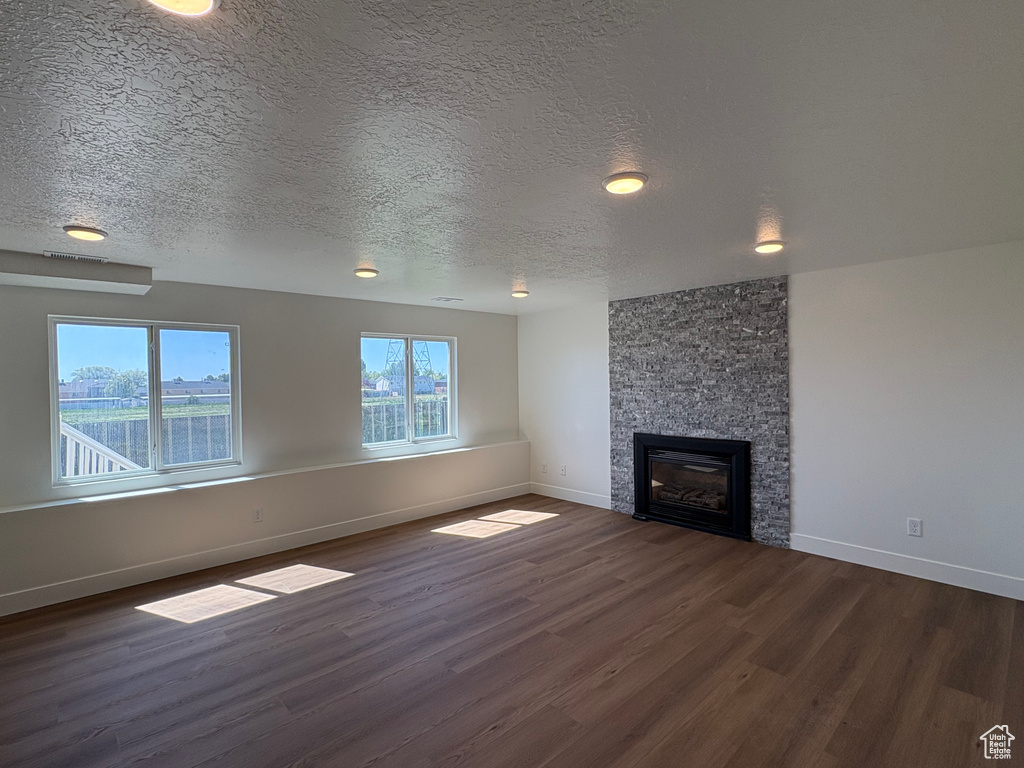 Unfurnished living room with visible vents, a fireplace, baseboards, dark wood-type flooring, and a textured ceiling
