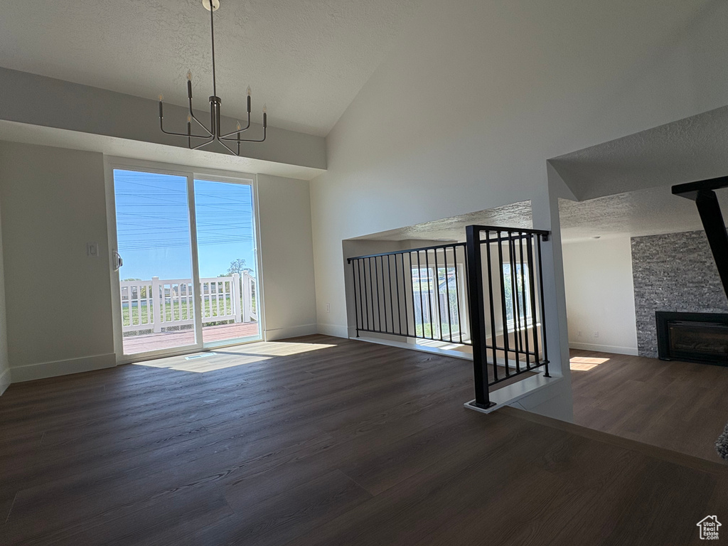 Unfurnished living room with wood finished floors, a fireplace, baseboards, high vaulted ceiling, and a textured ceiling