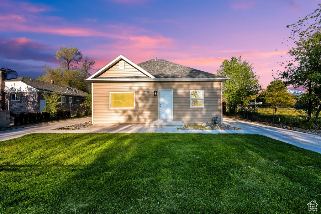 View of front of home with a yard, fence, and roof with shingles