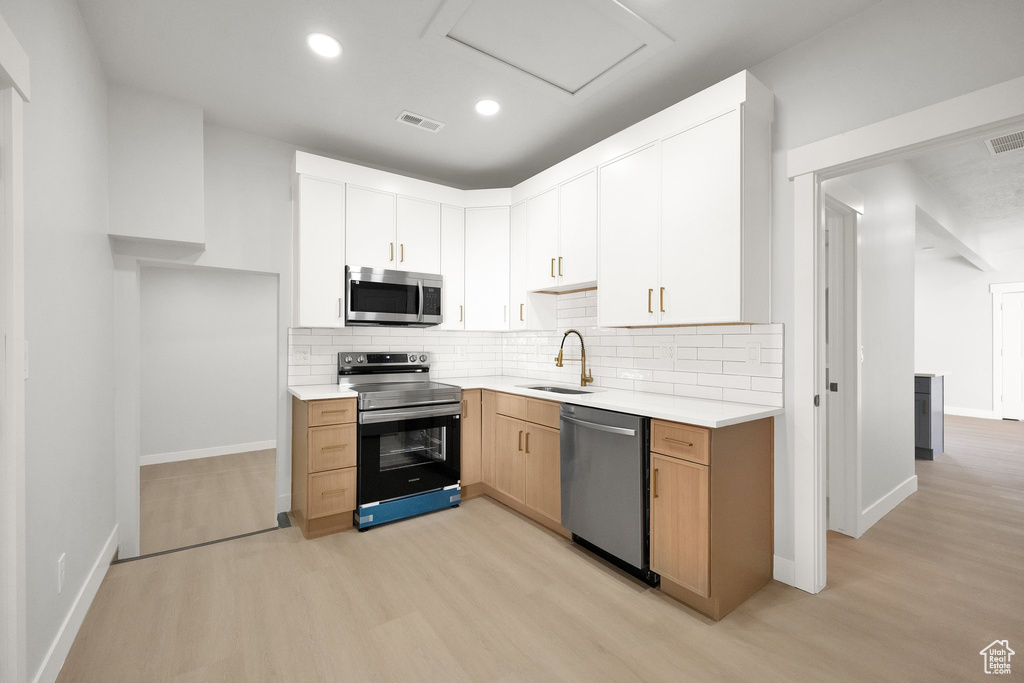 Kitchen featuring decorative backsplash, visible vents, appliances with stainless steel finishes, a sink, and light wood finished floors