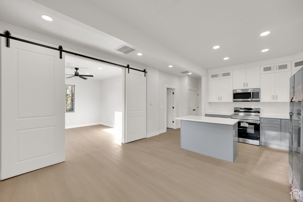 Kitchen with light wood-style floors, appliances with stainless steel finishes, a barn door, and visible vents
