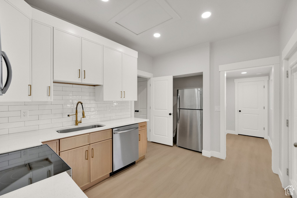 Kitchen with light wood-style floors, light countertops, a sink, appliances with stainless steel finishes, and backsplash