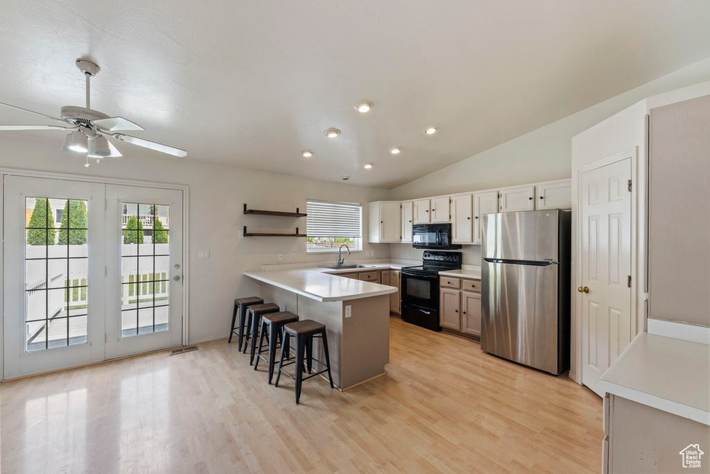 Kitchen featuring a breakfast bar, a sink, a peninsula, light wood-type flooring, and black appliances