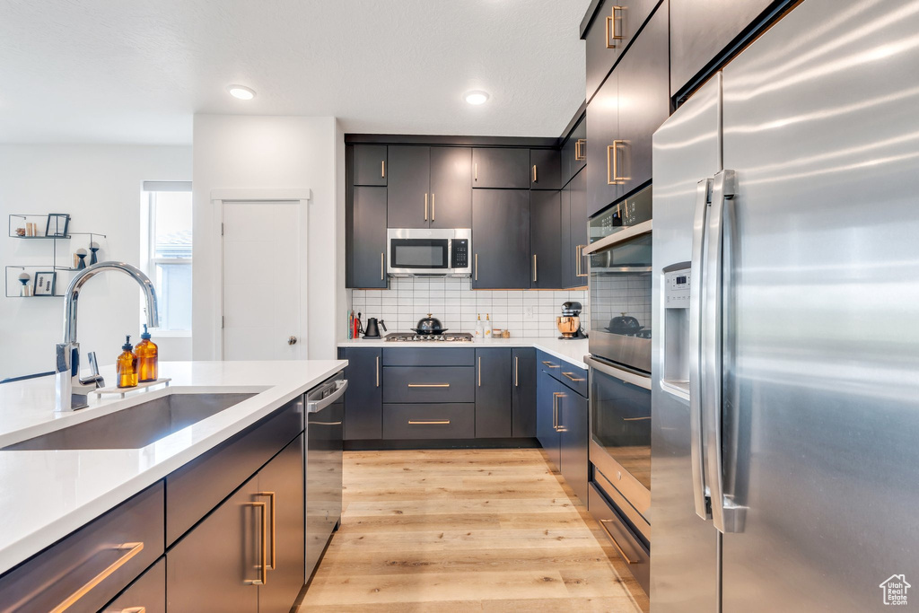 Kitchen featuring light countertops, tasteful backsplash, a sink, light wood finished floors, and appliances with stainless steel finishes