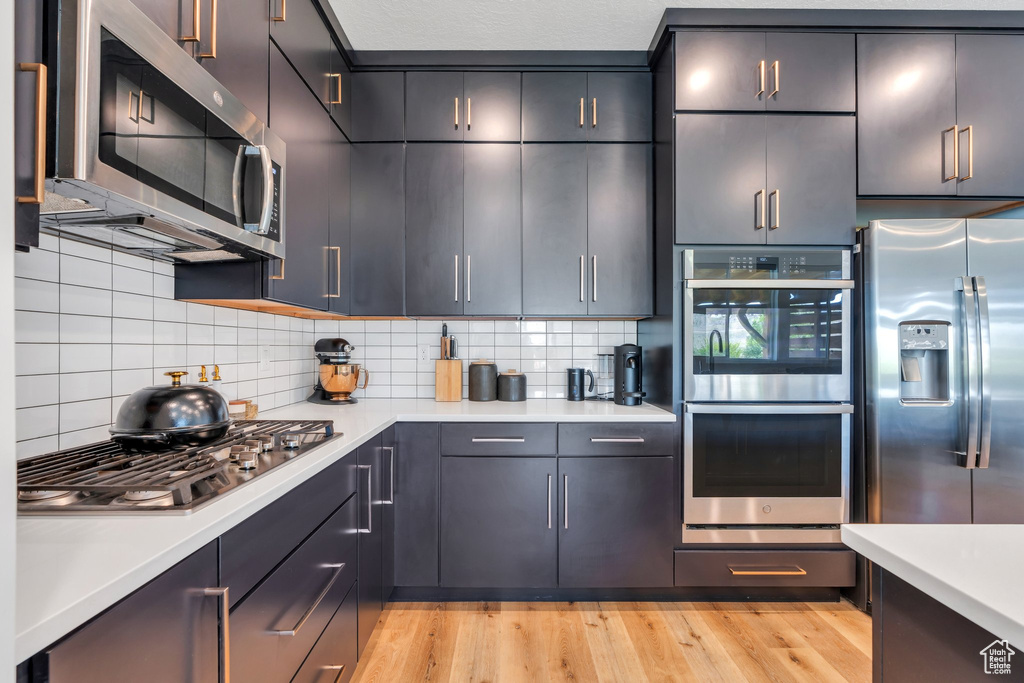 Kitchen featuring light countertops, appliances with stainless steel finishes, tasteful backsplash, and light wood finished floors