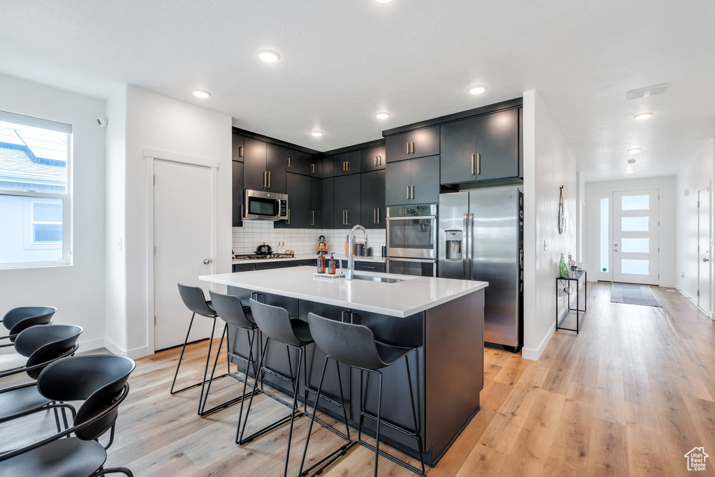 Kitchen featuring backsplash, a sink, light countertops, light wood-style floors, and stainless steel appliances
