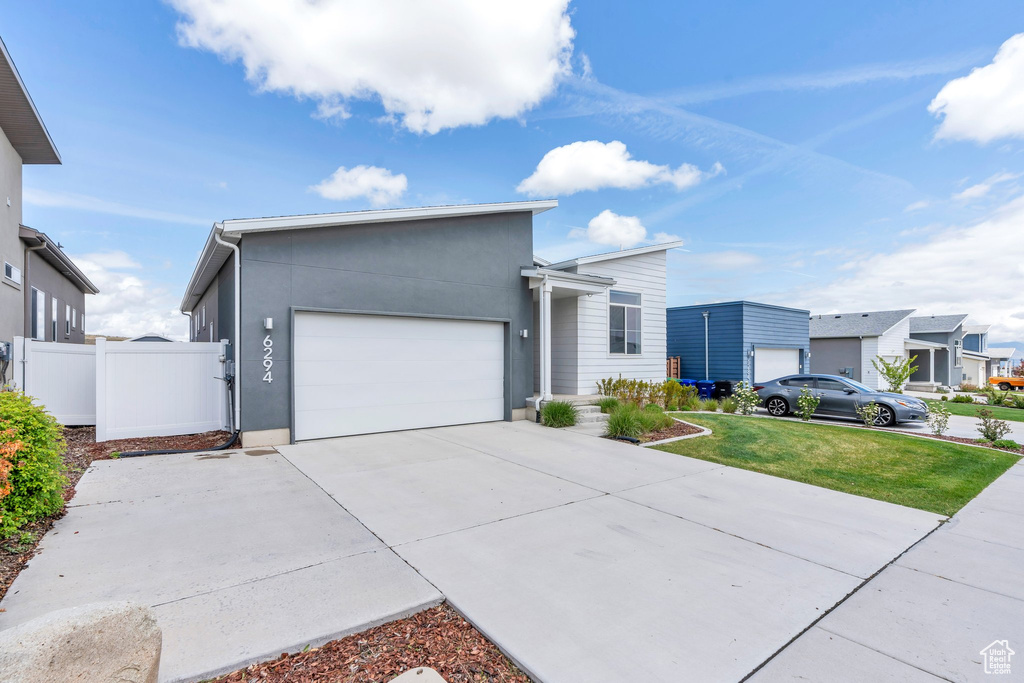 View of front of property with a front yard, fence, concrete driveway, an attached garage, and stucco siding