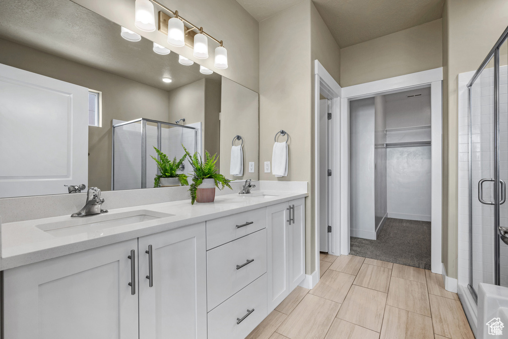 Bathroom featuring double vanity, a spacious closet, a shower stall, and a sink