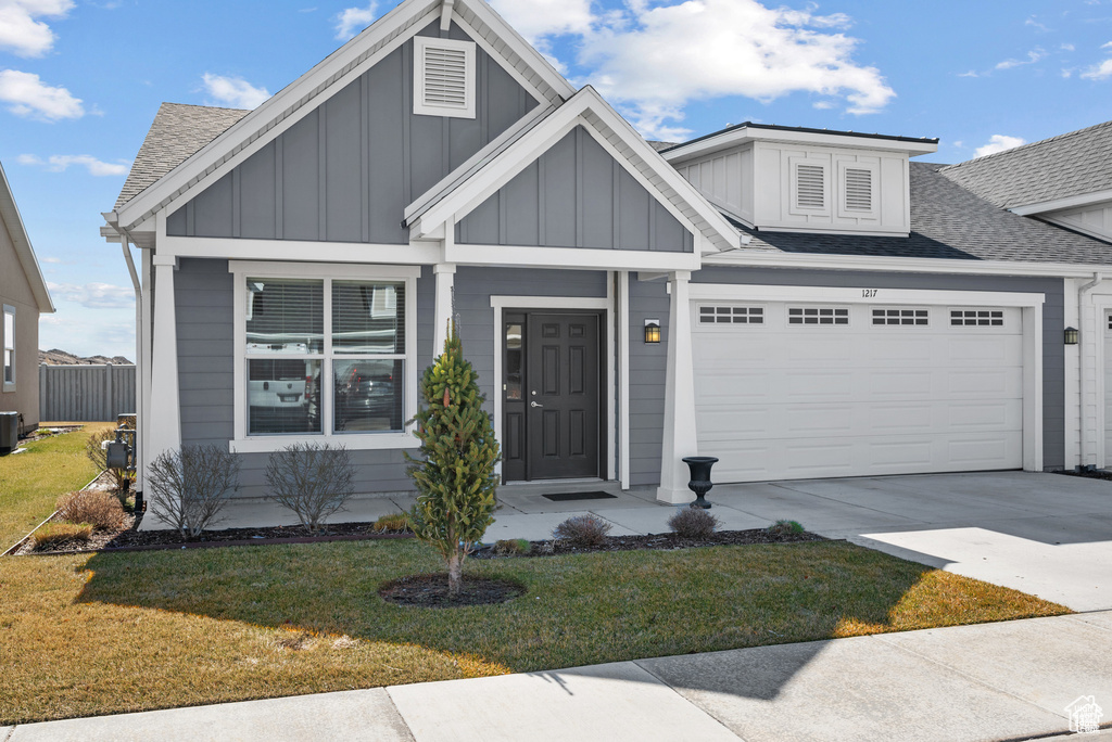 Craftsman-style house with board and batten siding, driveway, a garage, a front lawn, and a shingled roof