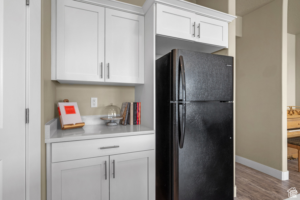 Kitchen with light countertops, white cabinets, freestanding refrigerator, and wood finished floors