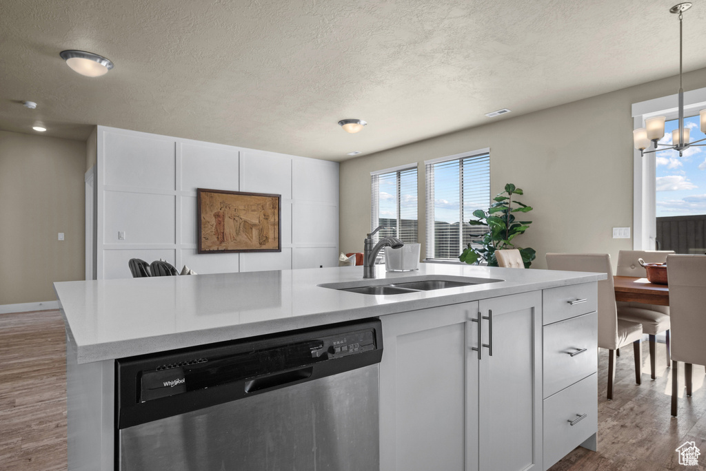 Kitchen with a textured ceiling, wood finished floors, dishwasher, a sink, and a notable chandelier