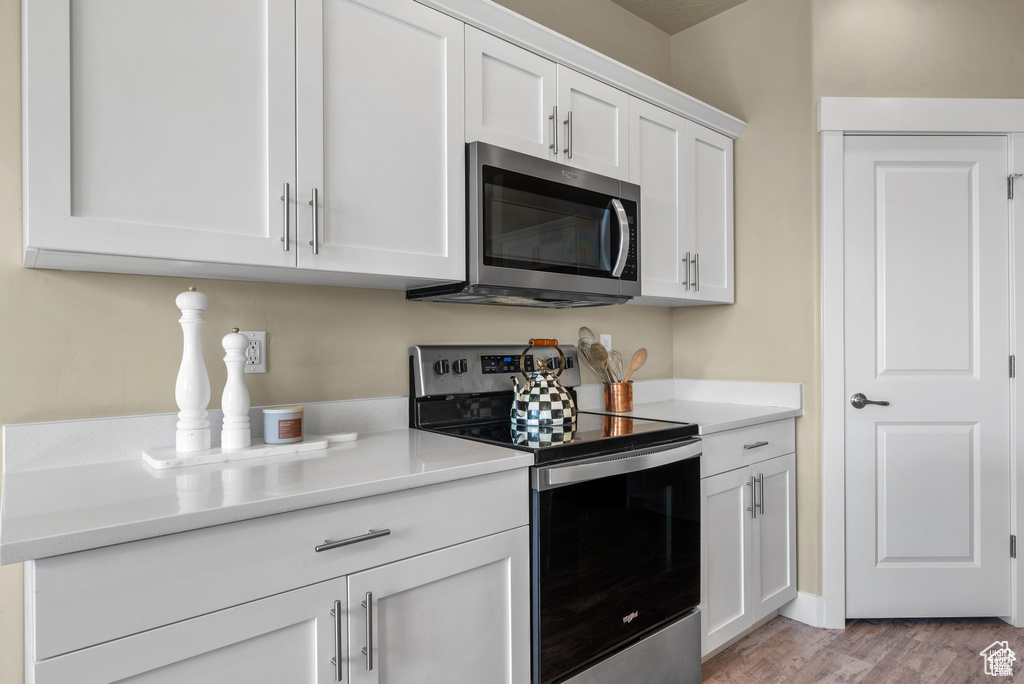 Kitchen with light wood-type flooring, light countertops, white cabinetry, and stainless steel appliances