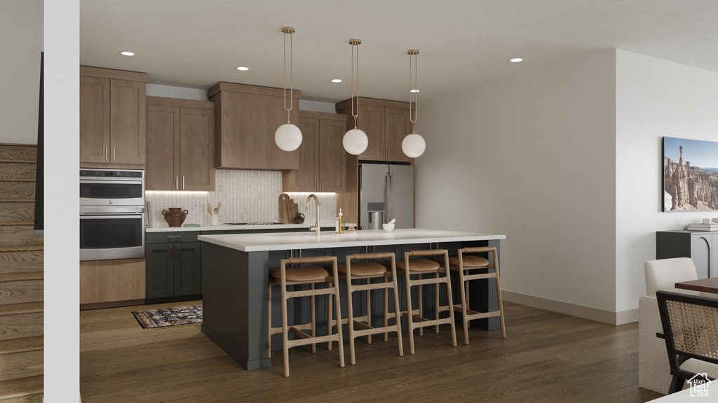 Kitchen with wood finished floors, a center island with sink, light countertops, tasteful backsplash, and stainless steel appliances